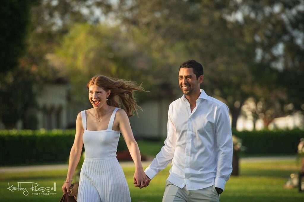 a man and woman holding hands and walking in a park
